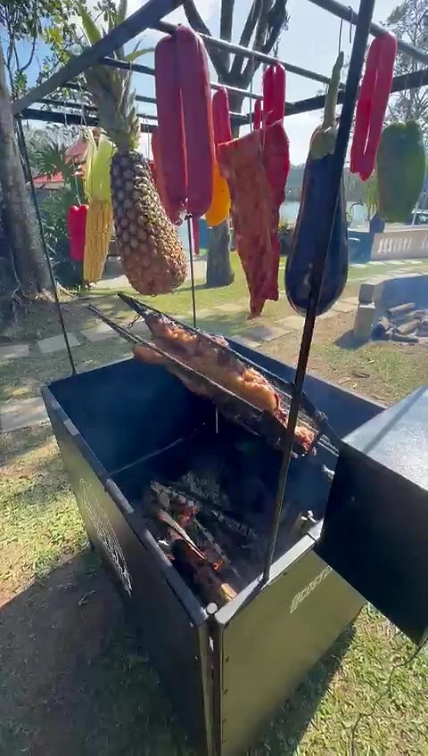 Vista de baixo do varal da Churrasqueira Rústica com abacaxi, linguiças e berinjela, e a costela assando logo abaixo